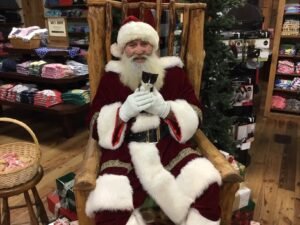 Santa sitting in a wooden chair, holding a black and white kitten.