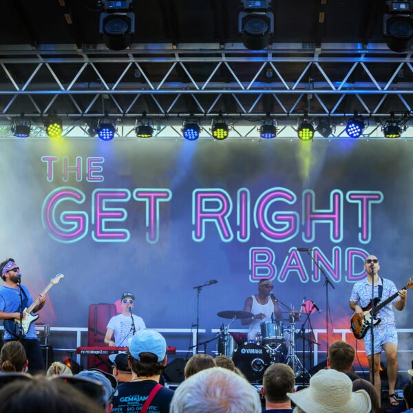 four men in a band on stage at a concert with "the get right band" behind them on the screen